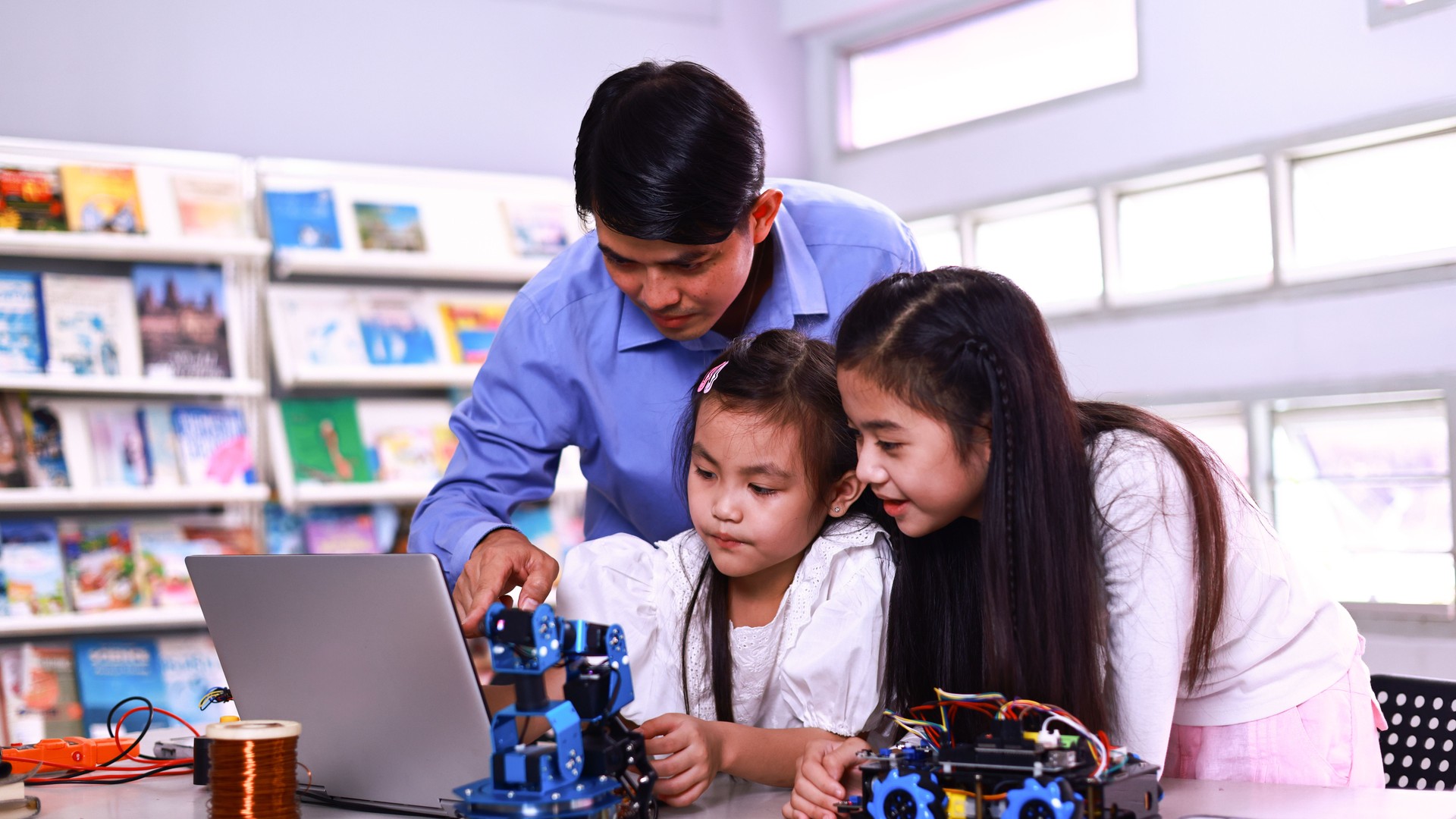young girls students building a robot, working with a wiring kit together with a male teacher at a stem robotics class. Inventions and creativity for kids